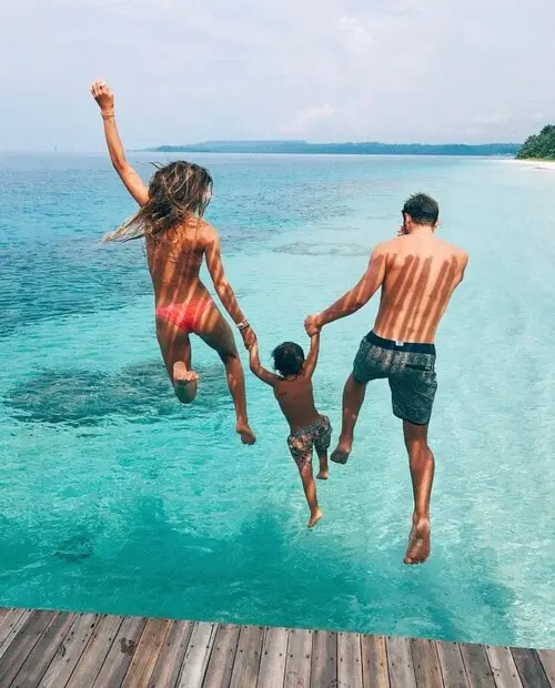 a happy family holding a kid and jumping in the sea