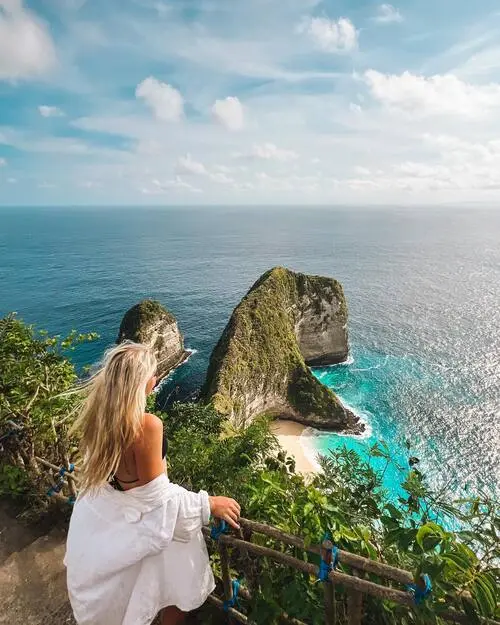 a woman holding a fence and looking at the sea