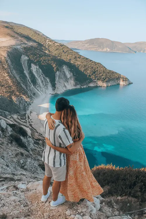 a couple standing on a mountain, hugging and looking at the sea