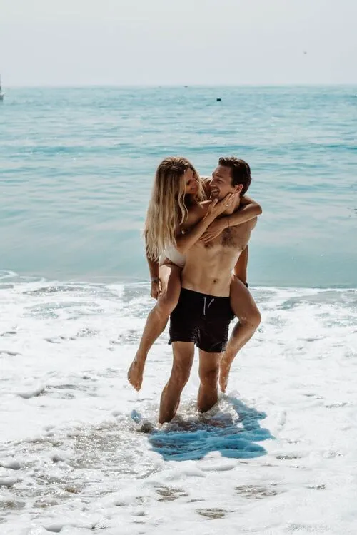a man standing on the seashore carrying a woman