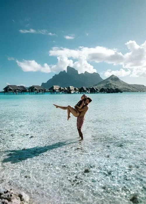 a man standing in shallow seawater picking up a woman