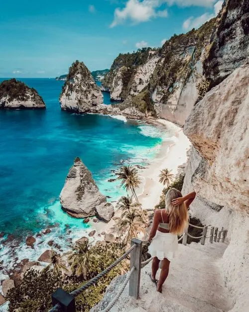 a woman holding a fence and looking at the sea